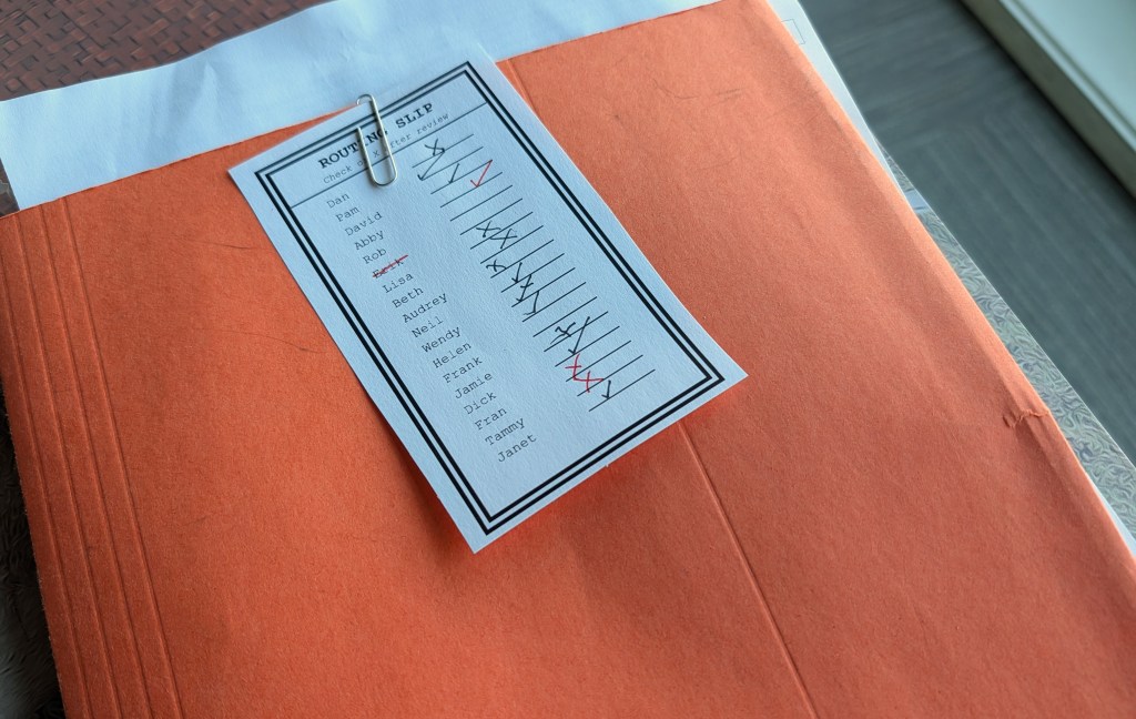 Orange folder with a paperclipped routing slip and 18 names with checkmarks. Only Rob's name lacks a checkmark.